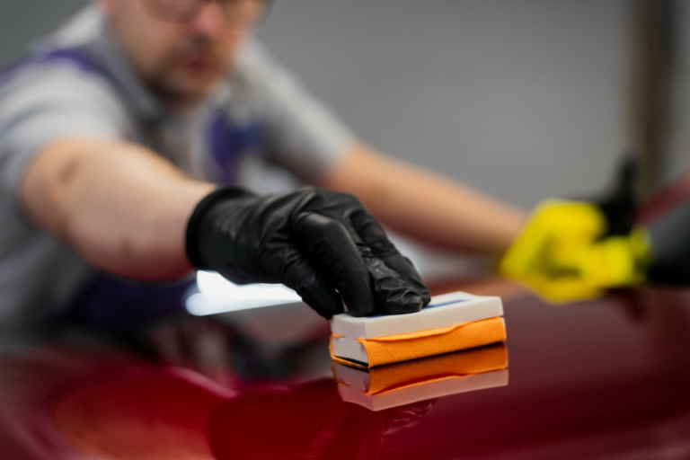 Close-up of a vehicle detailer applying ceramic coating on a red car during a detailing service